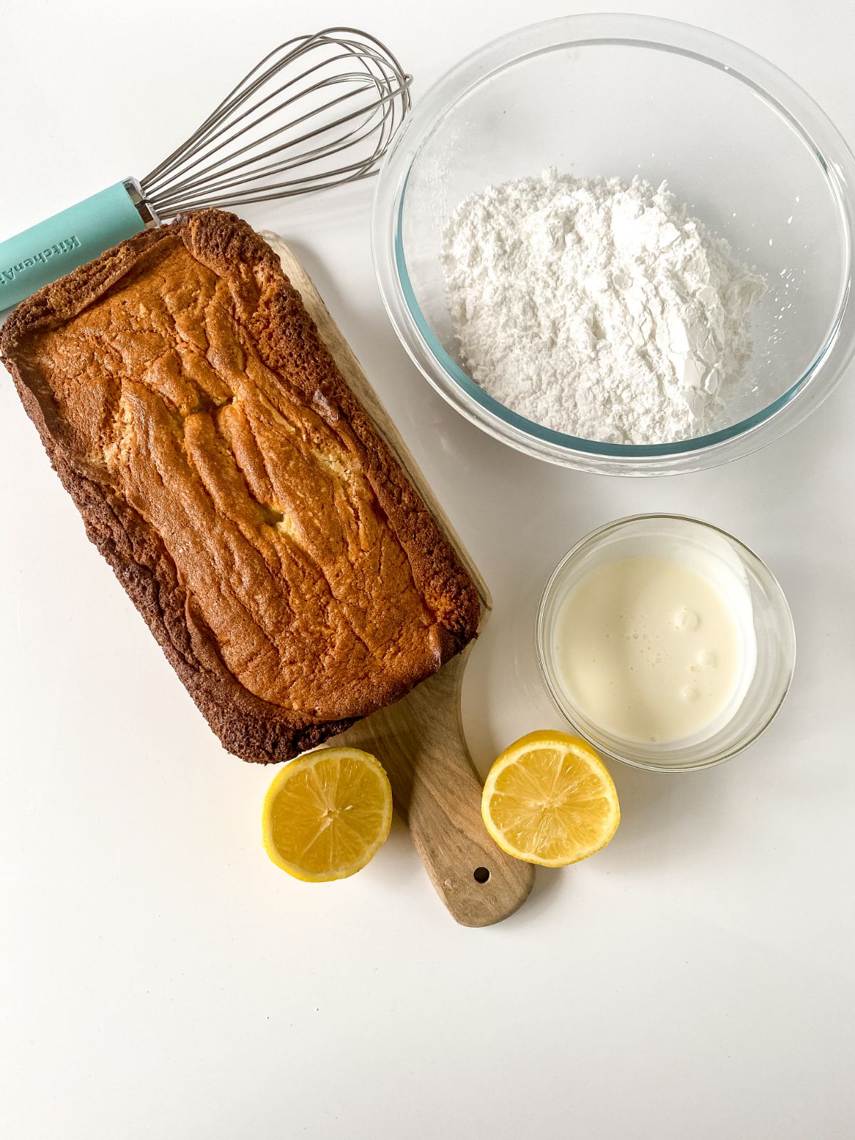 lemon loaf on cutting board beside ingredients for glaze