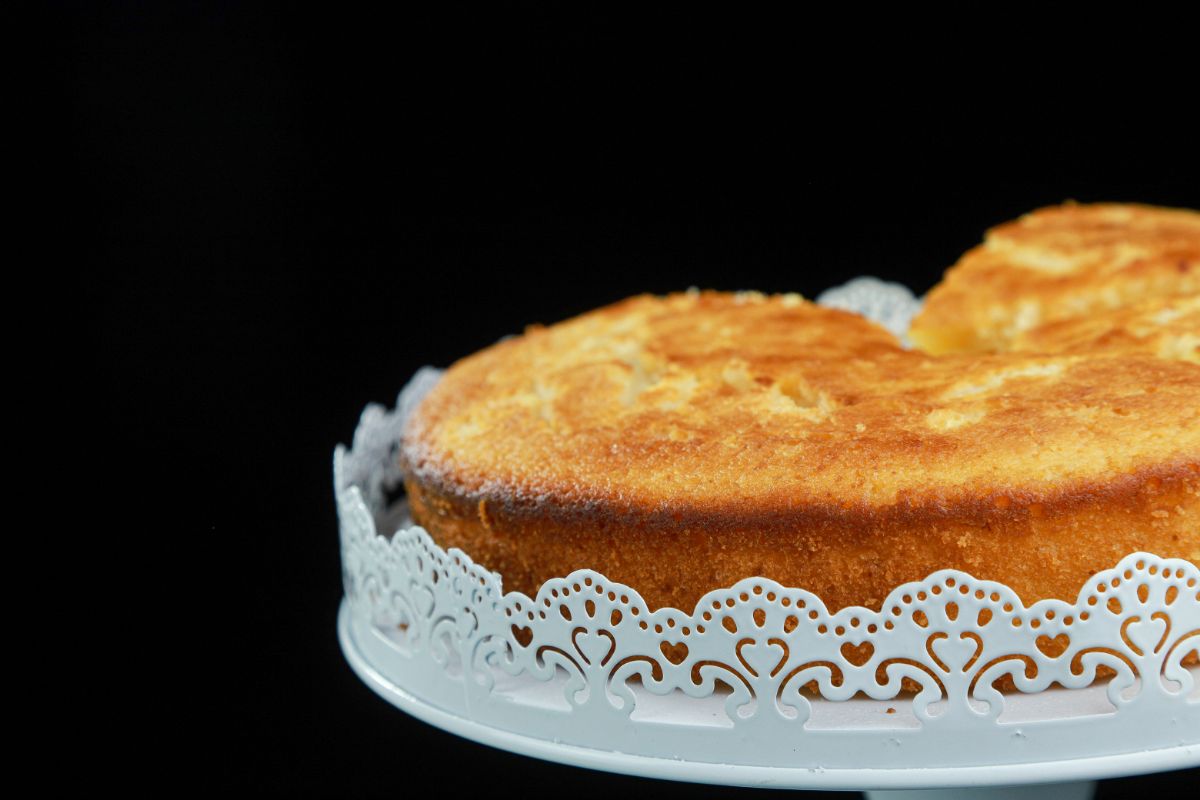white cake stand holding lemon cake in front of black background