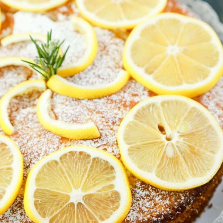 lemon olive oil cake on plate with sliced lemons on top