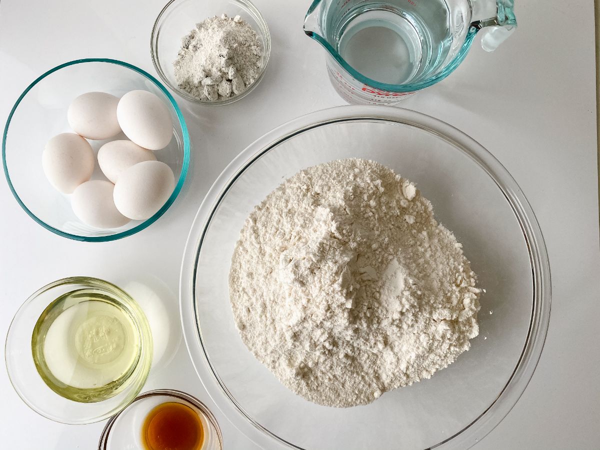 ingredients for baking a cake in large glass bowls on white table