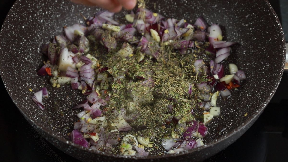 dry herbs being stirred into skillet with onions