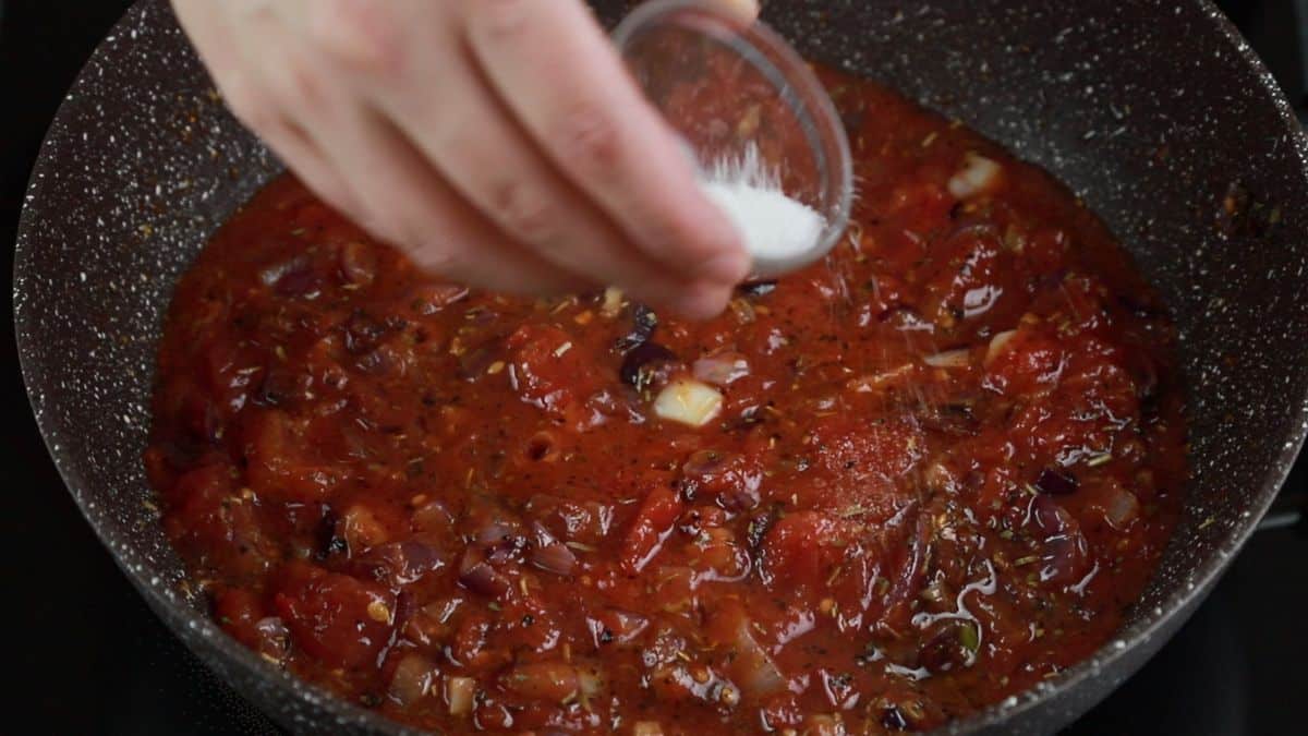 sugar being added to tomato sauce in skillet