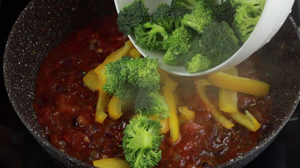 broccoli being poured into pan of pasta sauce