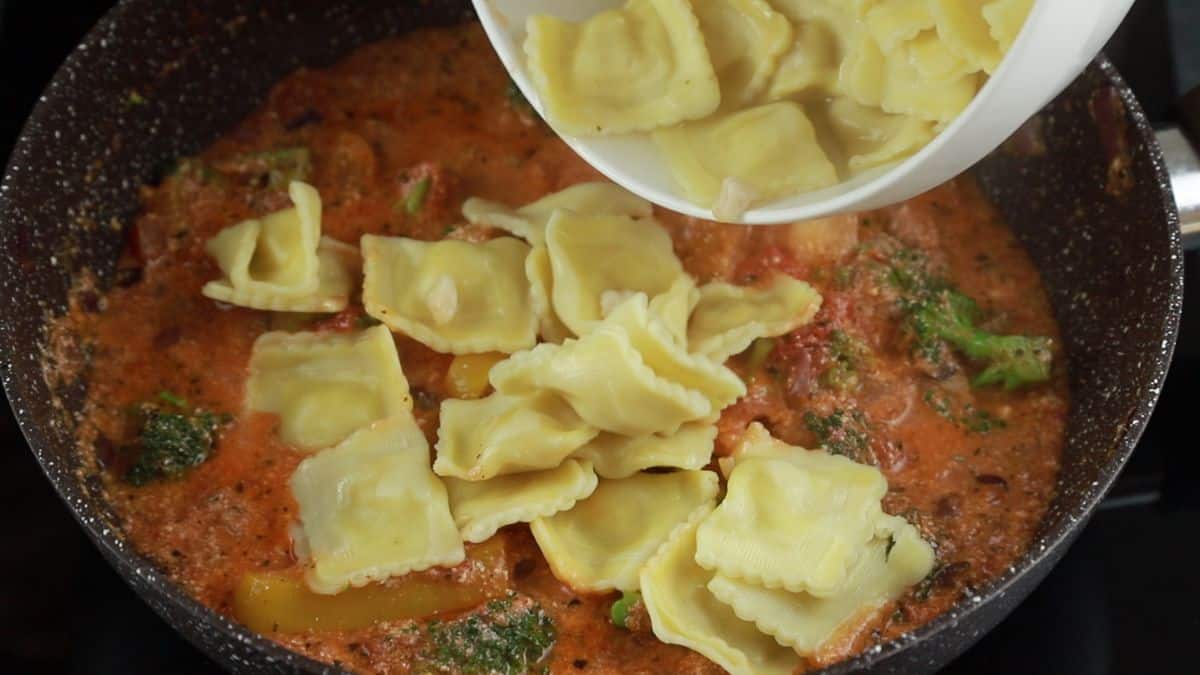 cooked ravioli being poured into skillet of red sauce