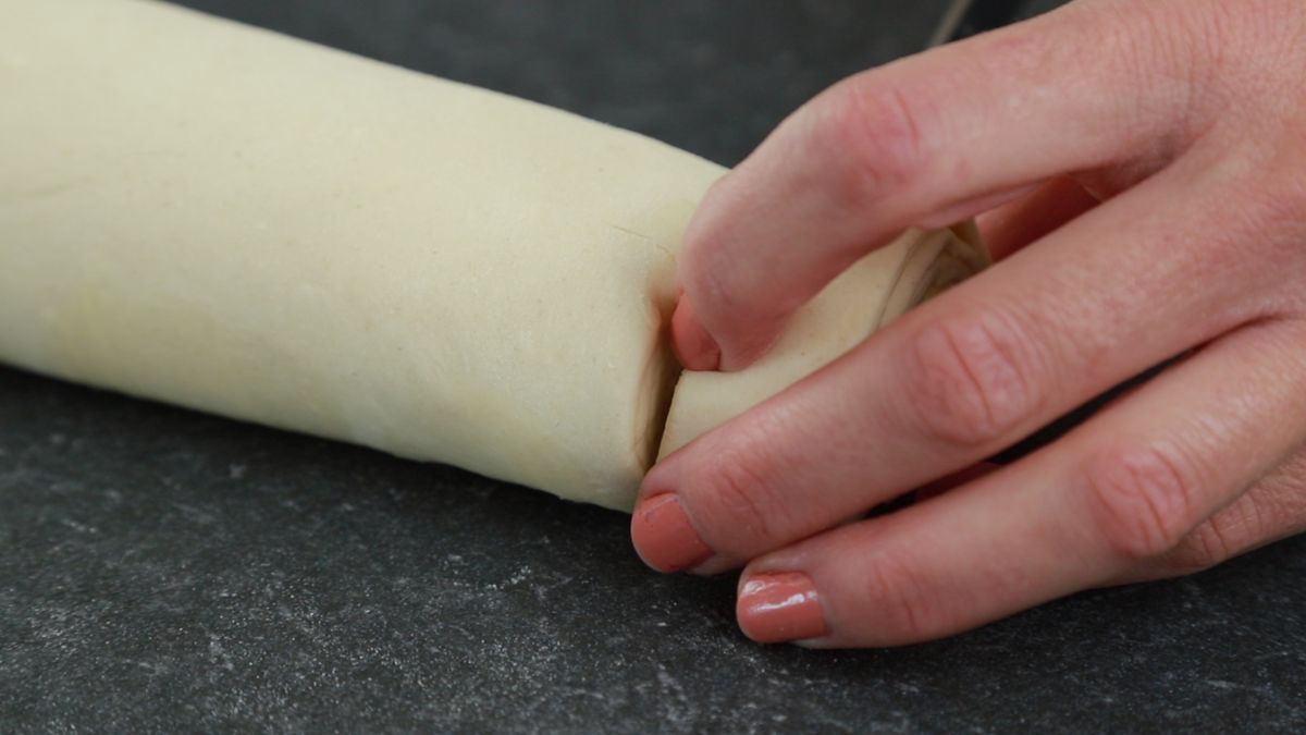 hand holding roll of pastry and slicing into rounds