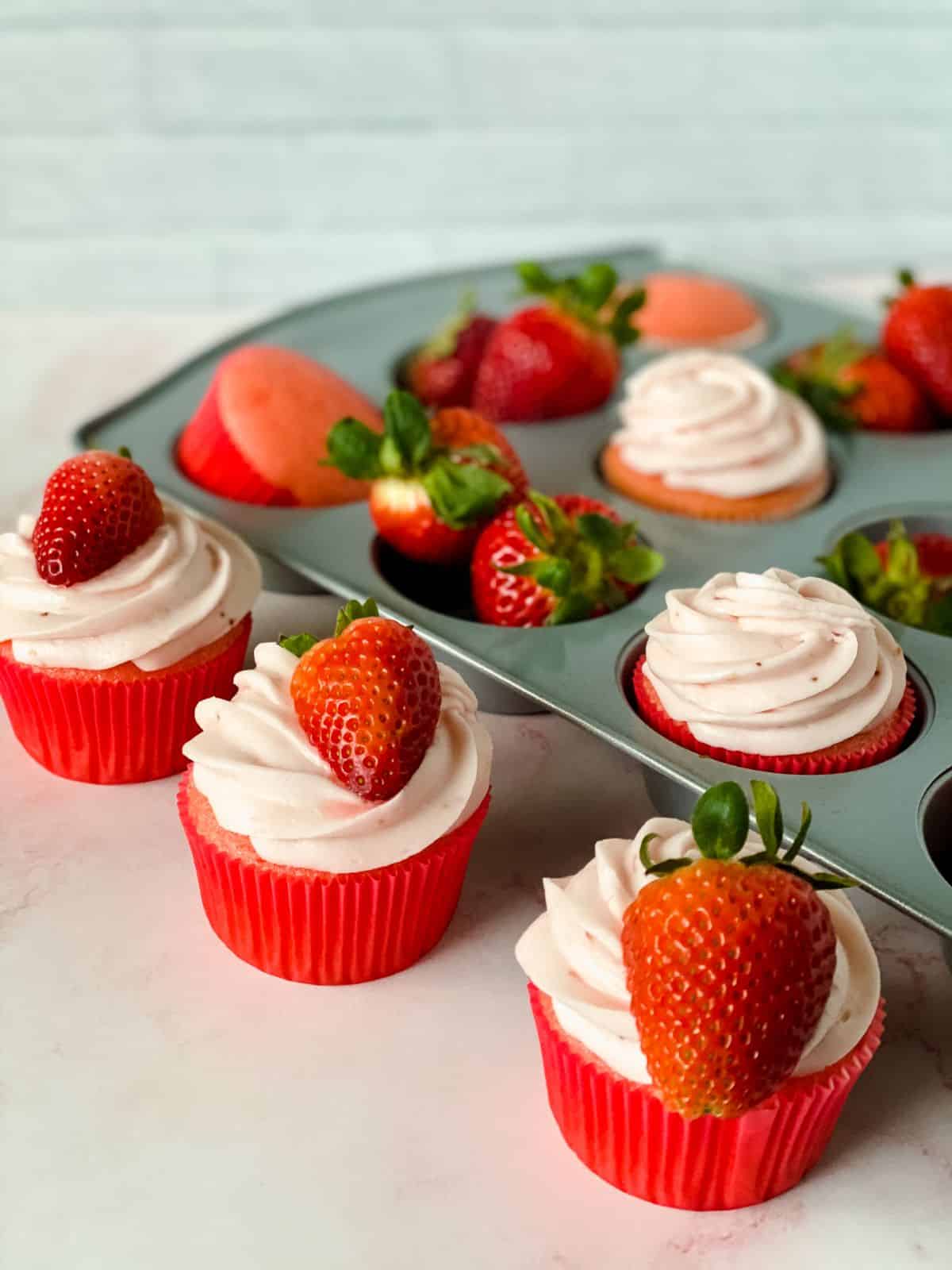 iced strawberry cupcakes on table by baking tin