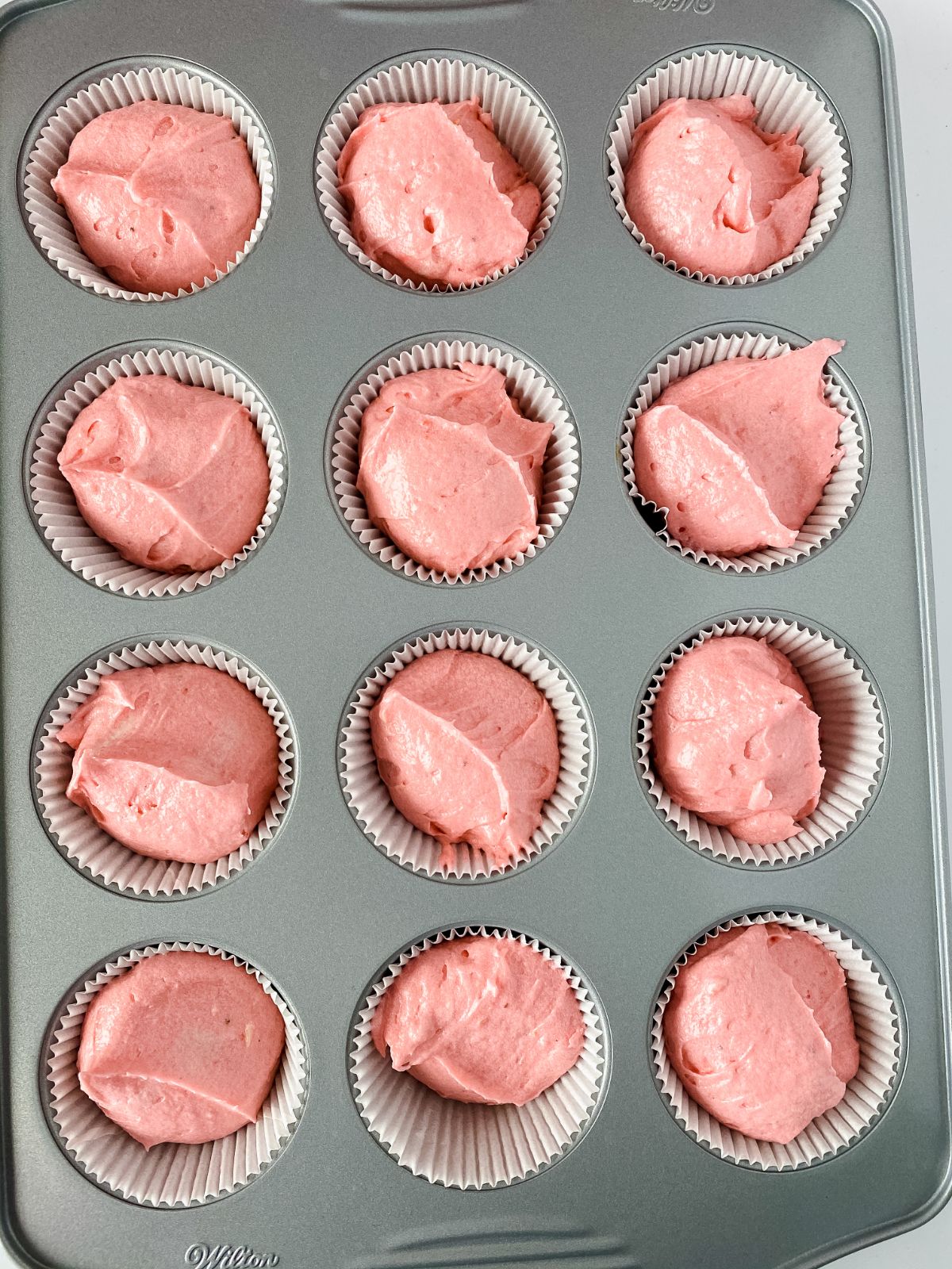 cupcake pan with strawberry cupcake batter in each liner