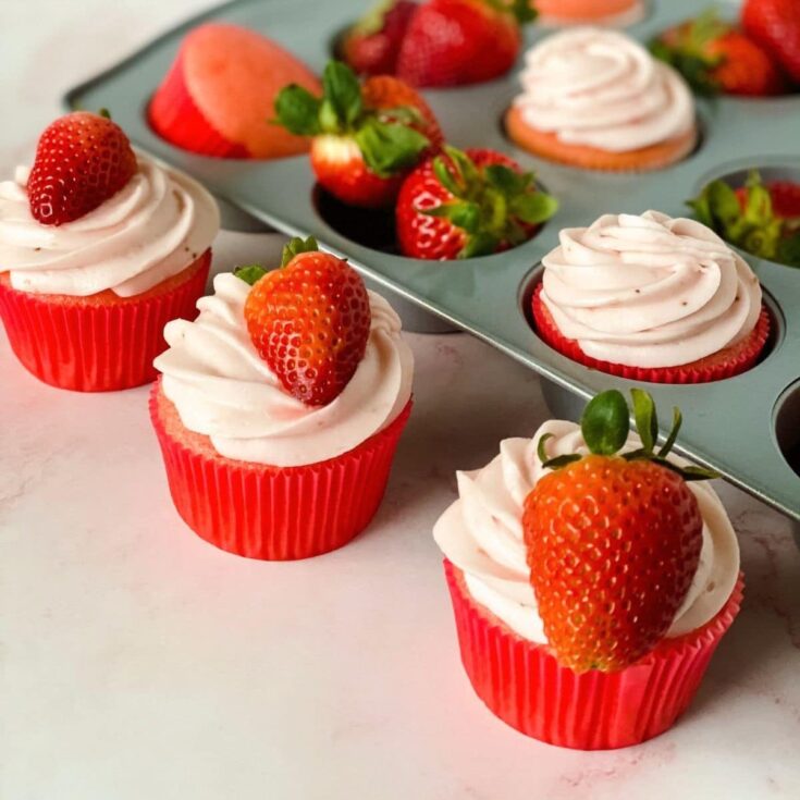 three strawberry cupcakes on table by cupcake pan