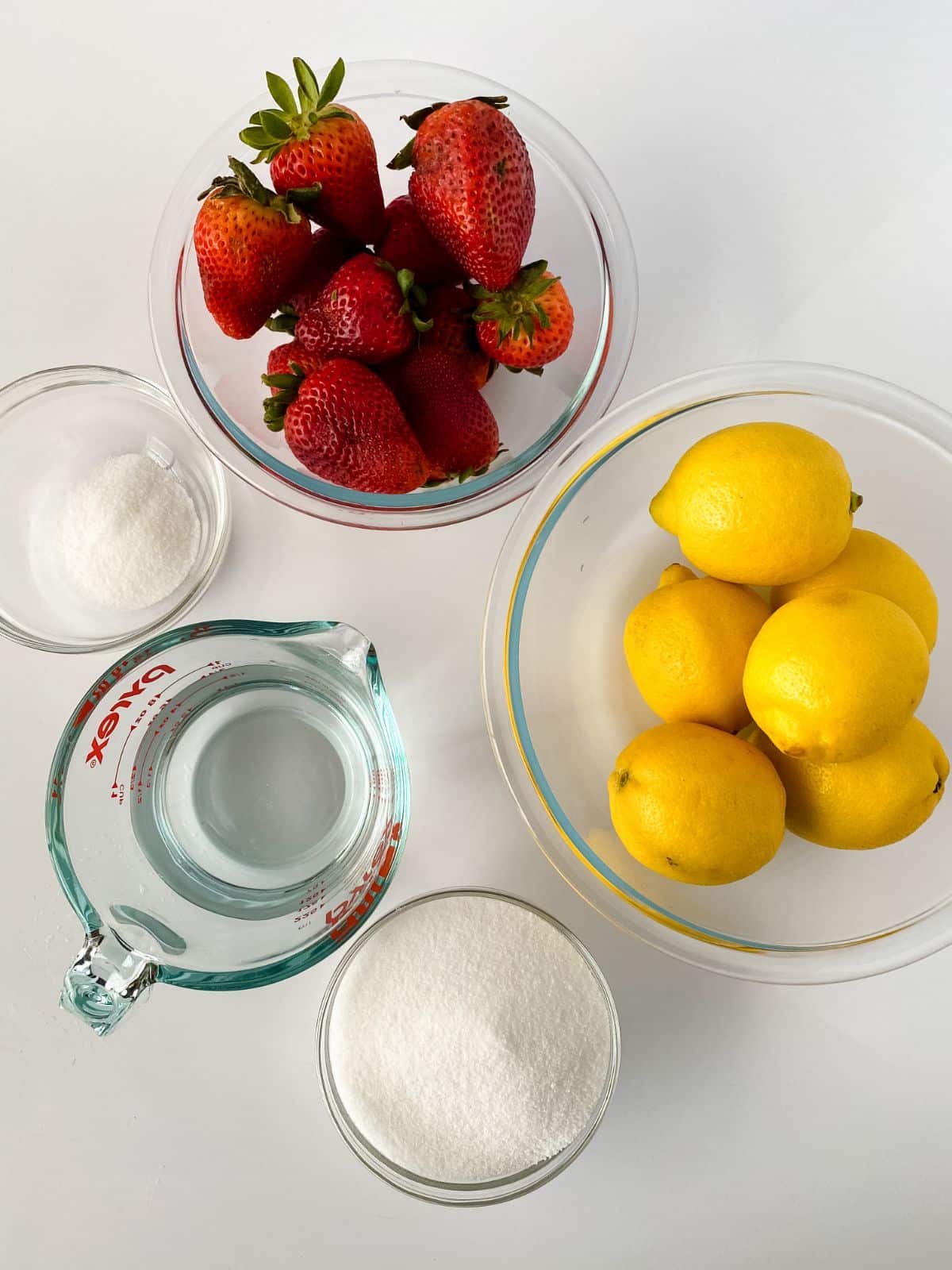 glass bowls holding lemons and strawberries on white table