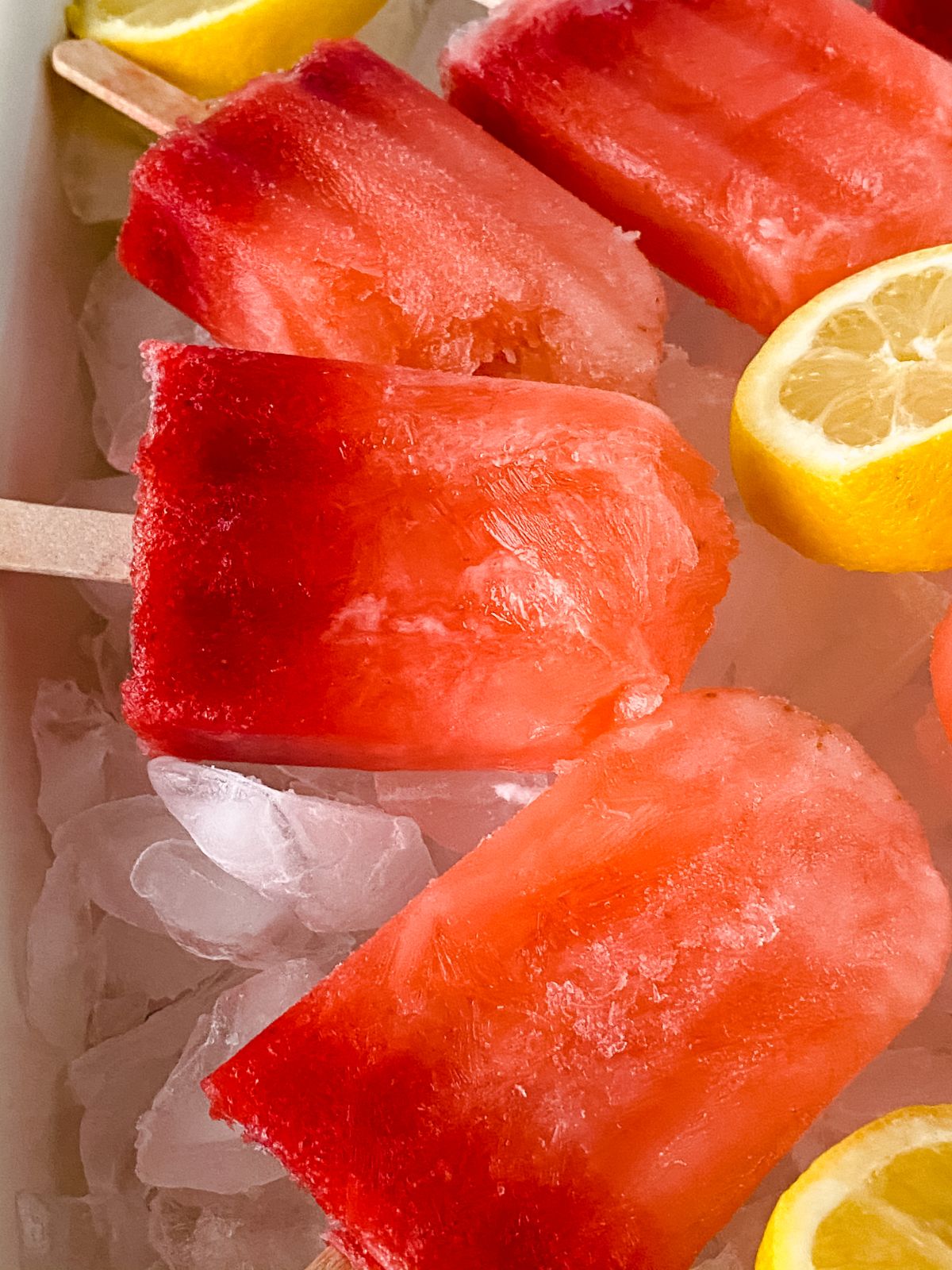 two toned pink strawberry lemonade popsicles on ice by lemon slice