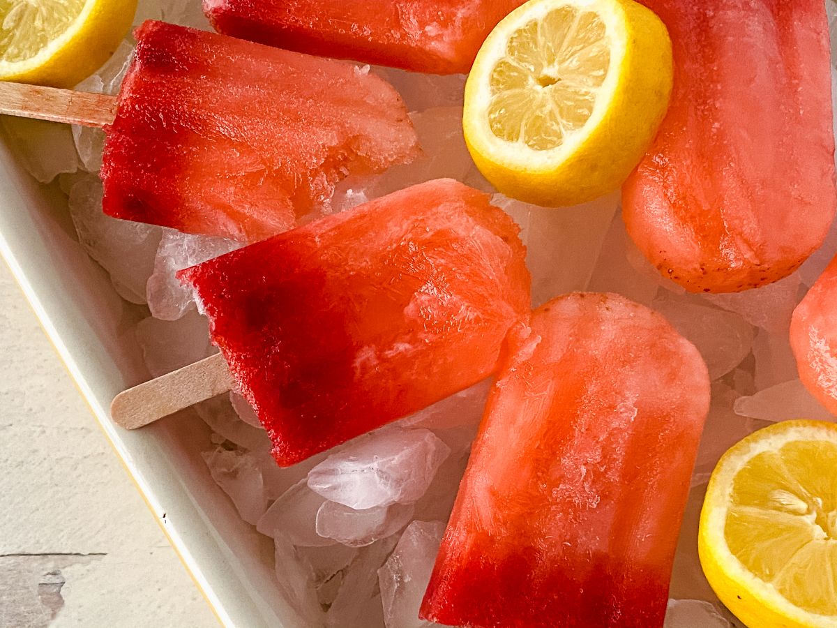 strawberry lemonade popsicles in white bowl with ice and lemon slices