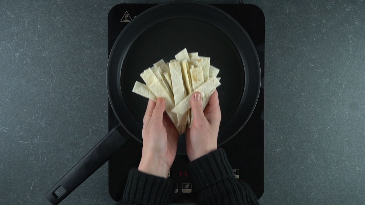hand putting tortilla strips into hot oil in black skillet