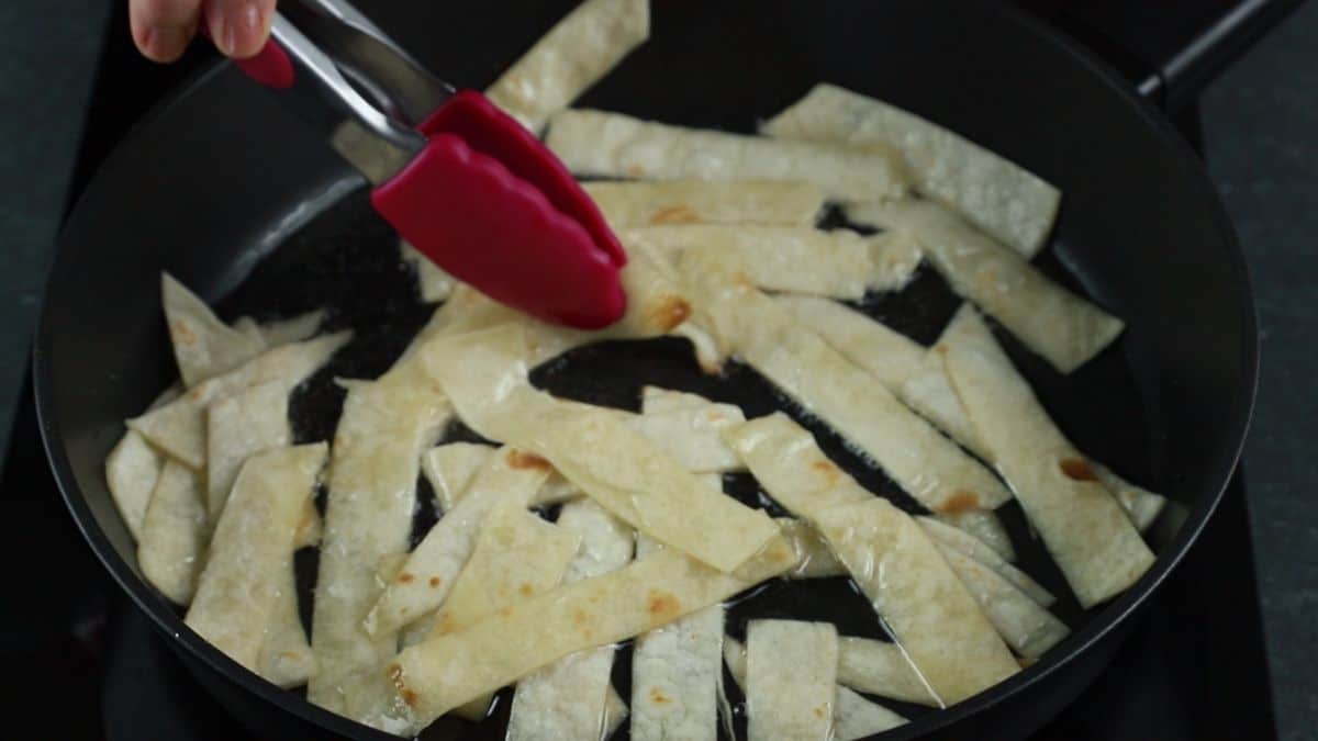 pink tongs pulling tortilla strips from skillet