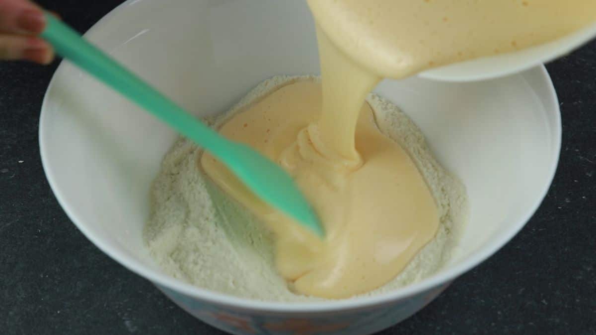 wet ingredients being poured into dry in a large white bowl