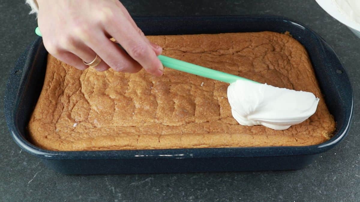 blue spatula spreading whipped cream over cake