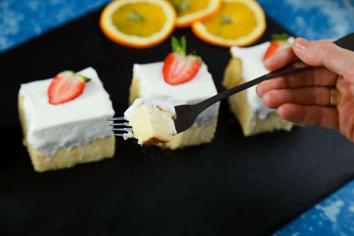 hand holding a fork of cake above a plate of three pieces of tres leches cake