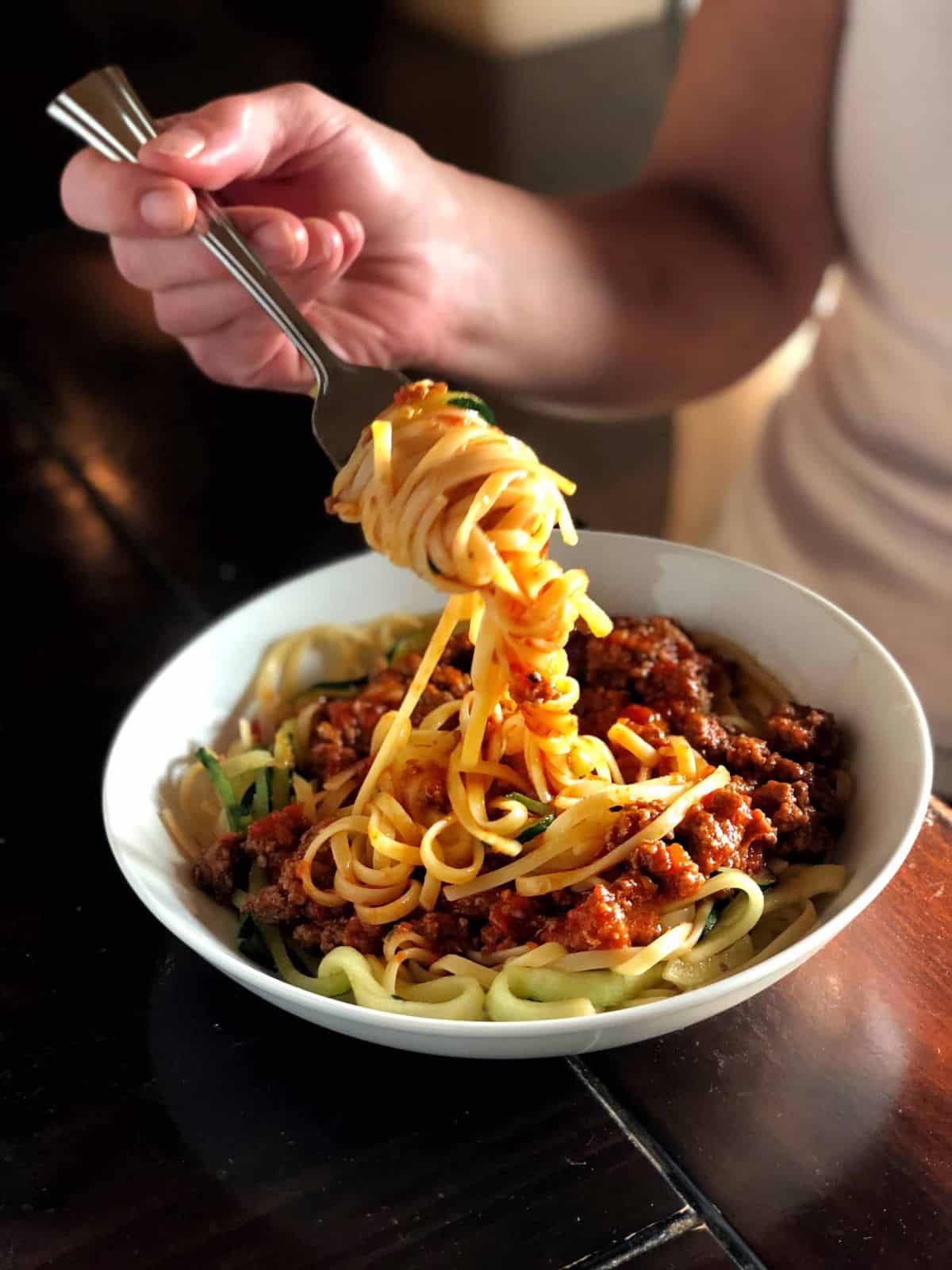 A woman with a fork eating a Pork Bolognese on a white plate.
