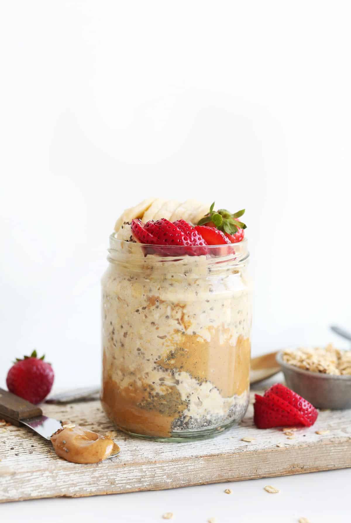 Overnight Oats with slices of banana, strawberries in a glass cup on a wooden cutting board.