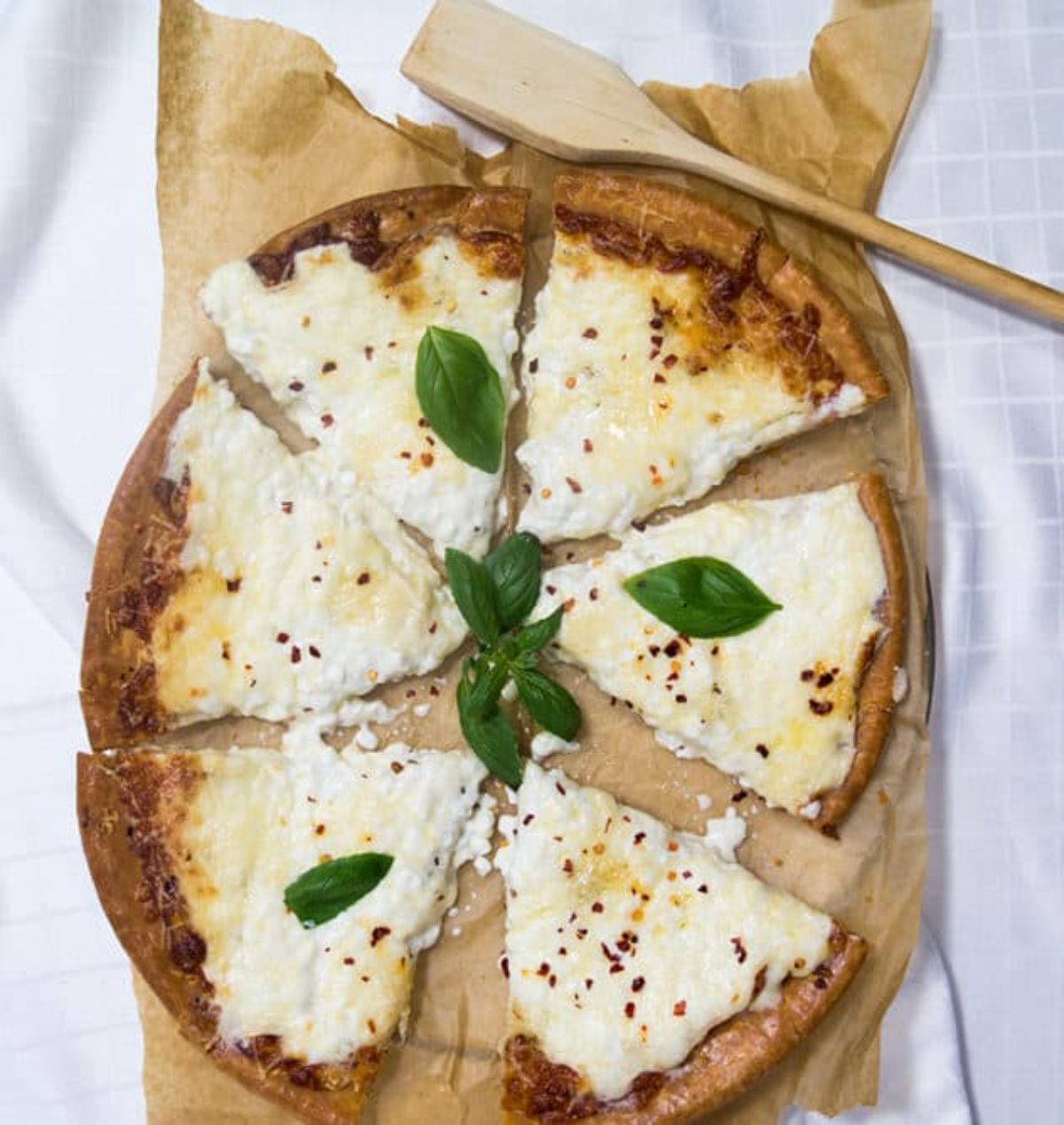 Sliced Cottage Cheese Pizza on a parchment papaer with a wooden spatula.