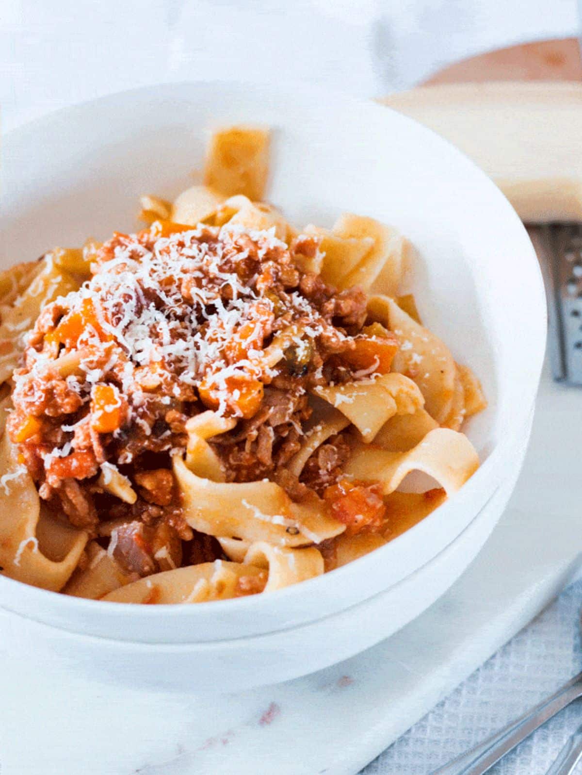 Pork Ragu with sliced cheese on the top in a white bowl.