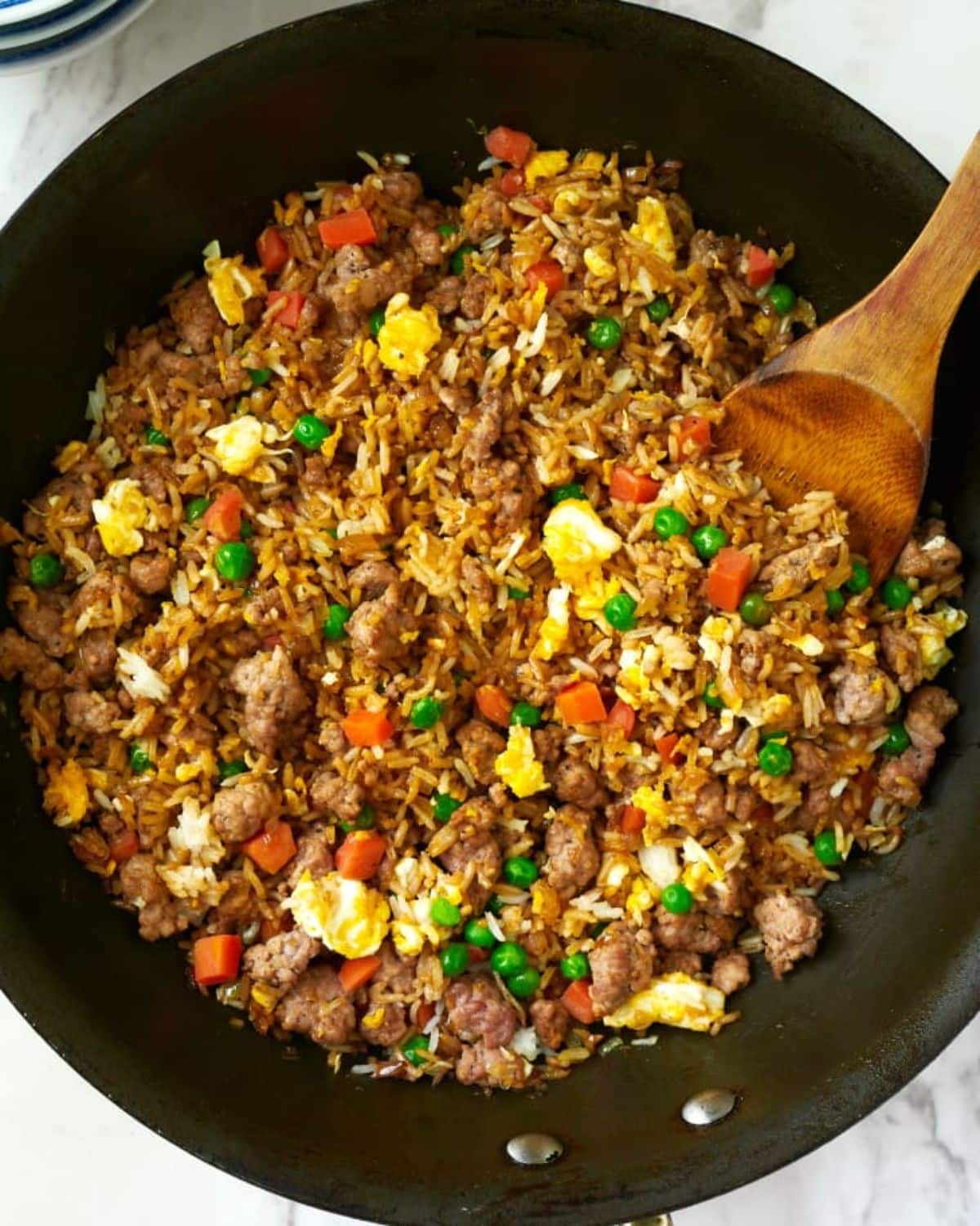 Pork Fried Rice in a black pan with a wooden spatula.