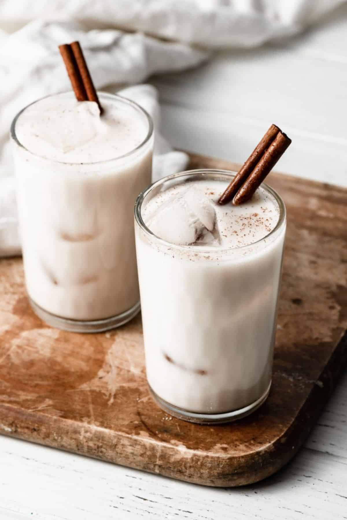 Horchata mexican dessert in two glass cups with cinnamon sticks on a wooden board.