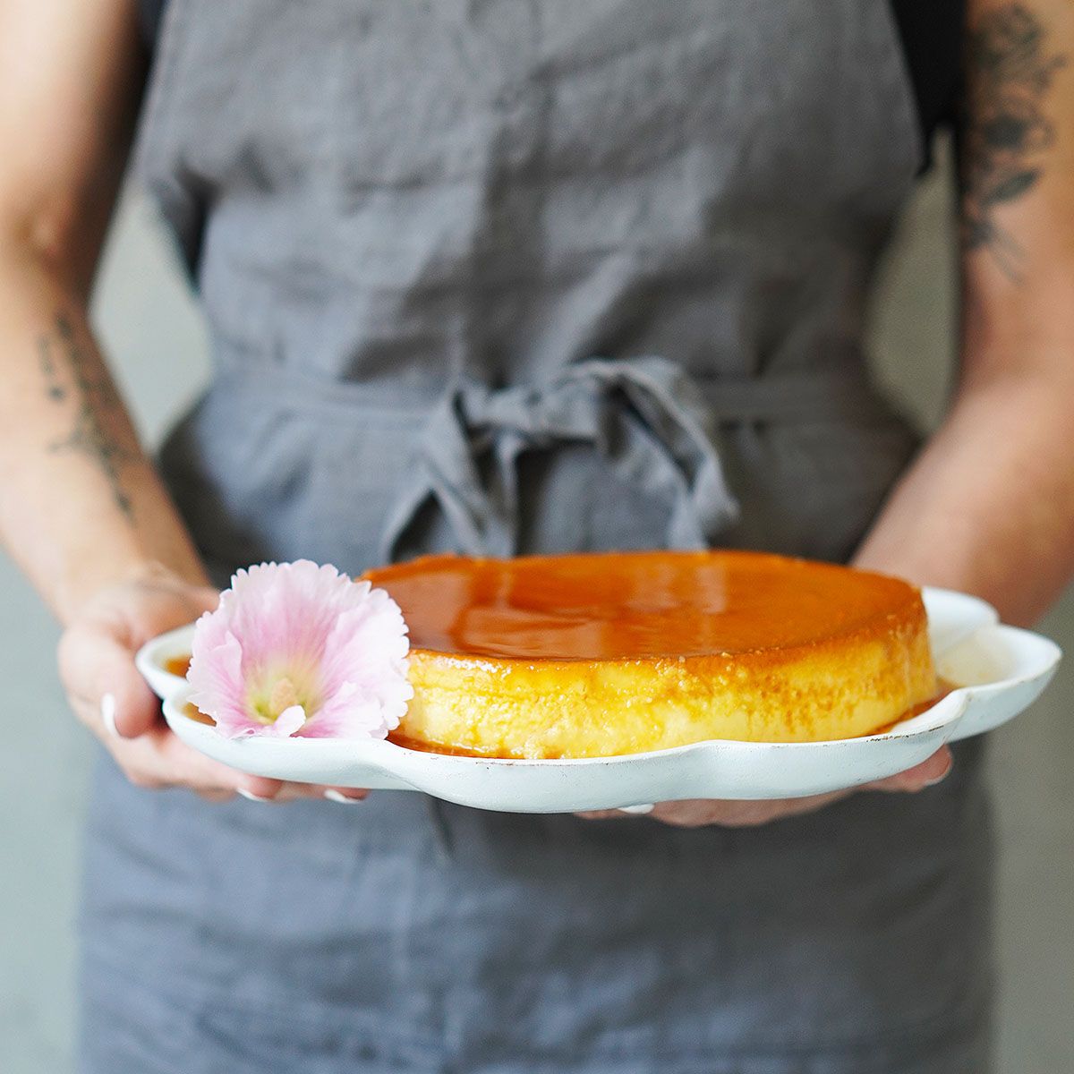 A woman holding a white tray with a flower and a Flan mexican dessert.