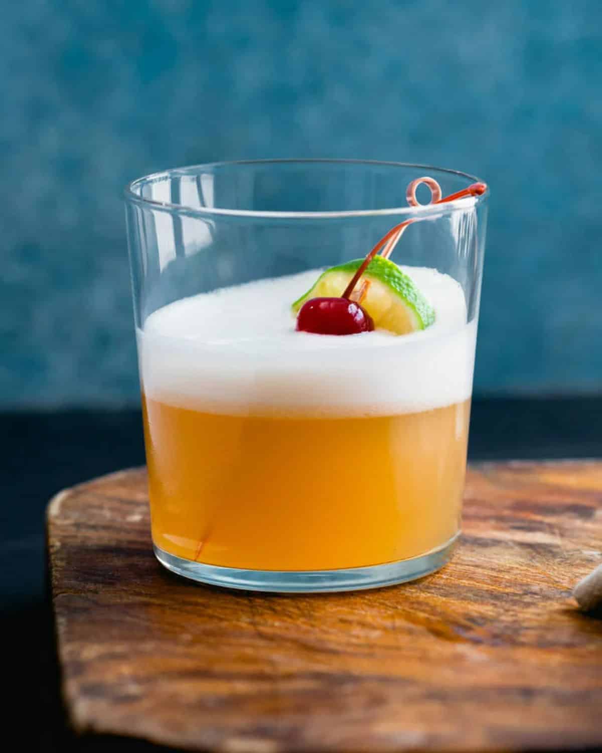 Tequila Sour cocktail with a slice of lime, a cherry in a glass cup.