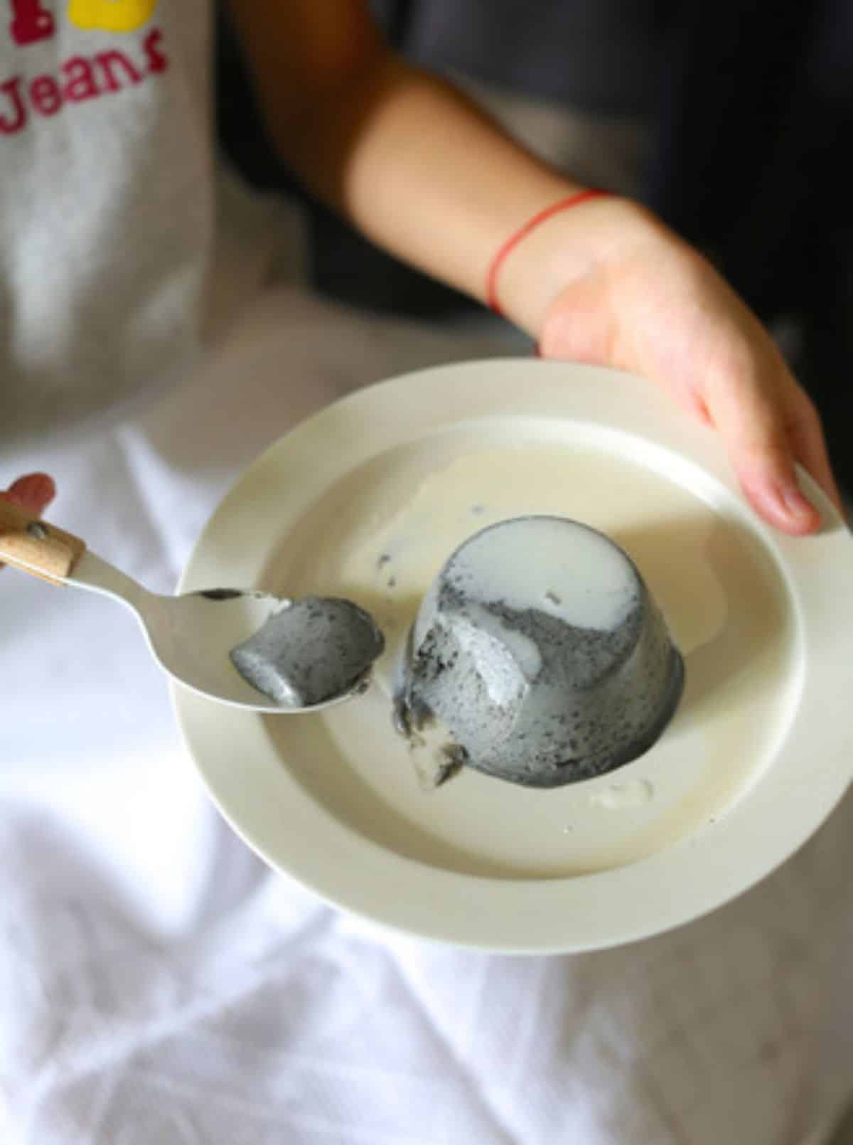 Black Sesame Pudding on a white plate picked by a spoon held by a chef.