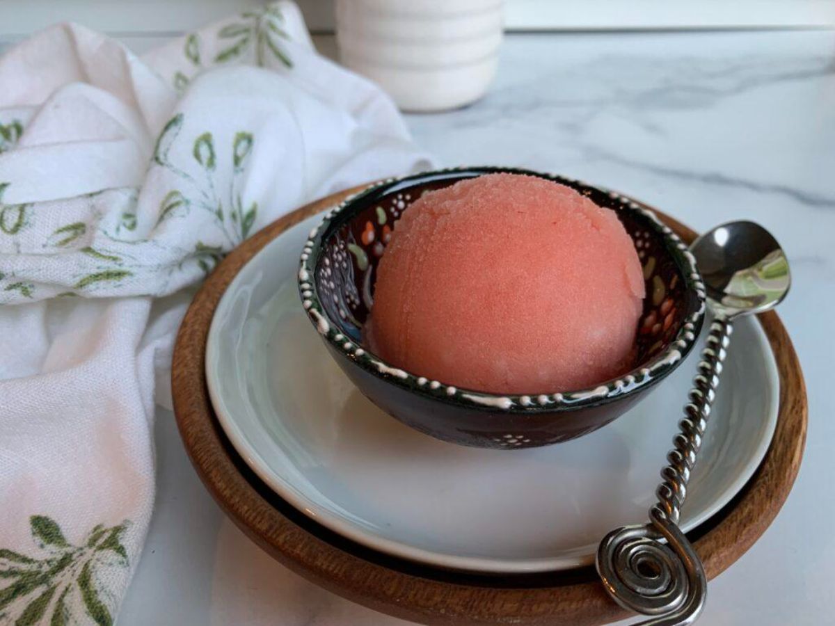 Watermelon Lime Sorbet in a black bowl on a plate with a spoon.