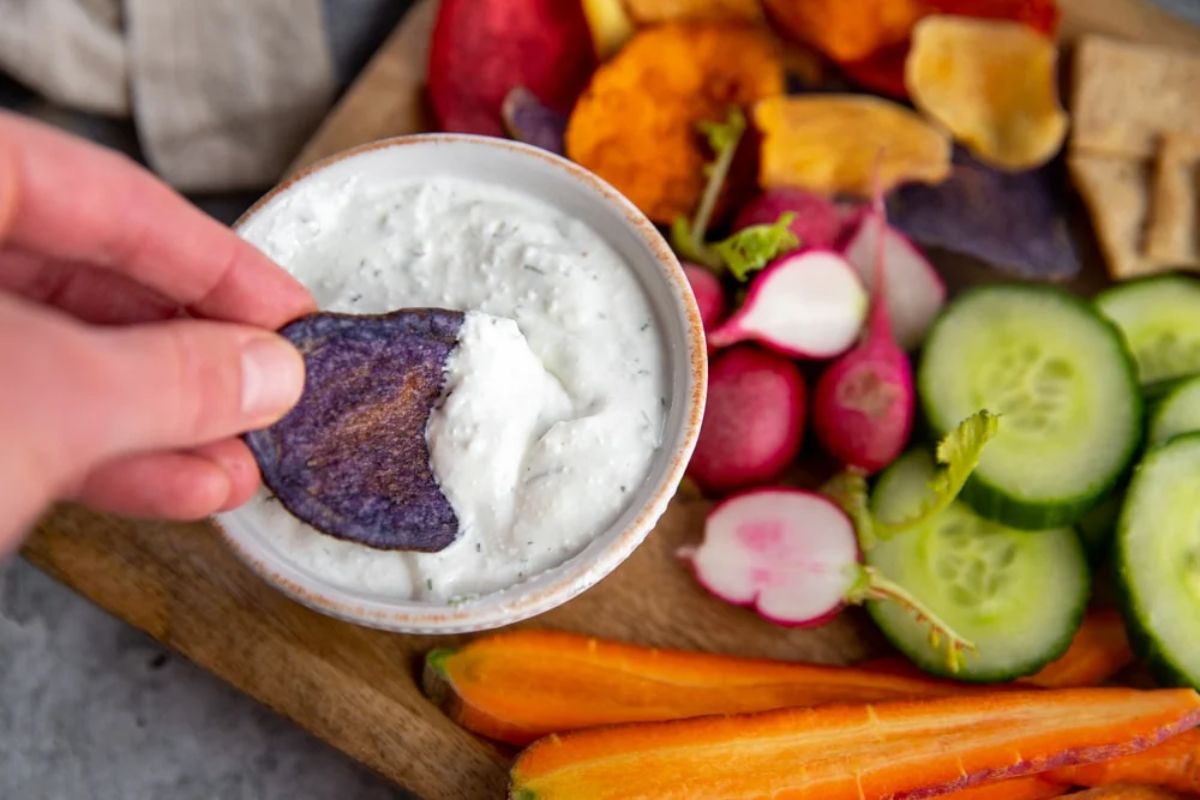 Whipped Cottage Cheese Dip in a small bowl on a wooden cutting board with sliced vegetables.