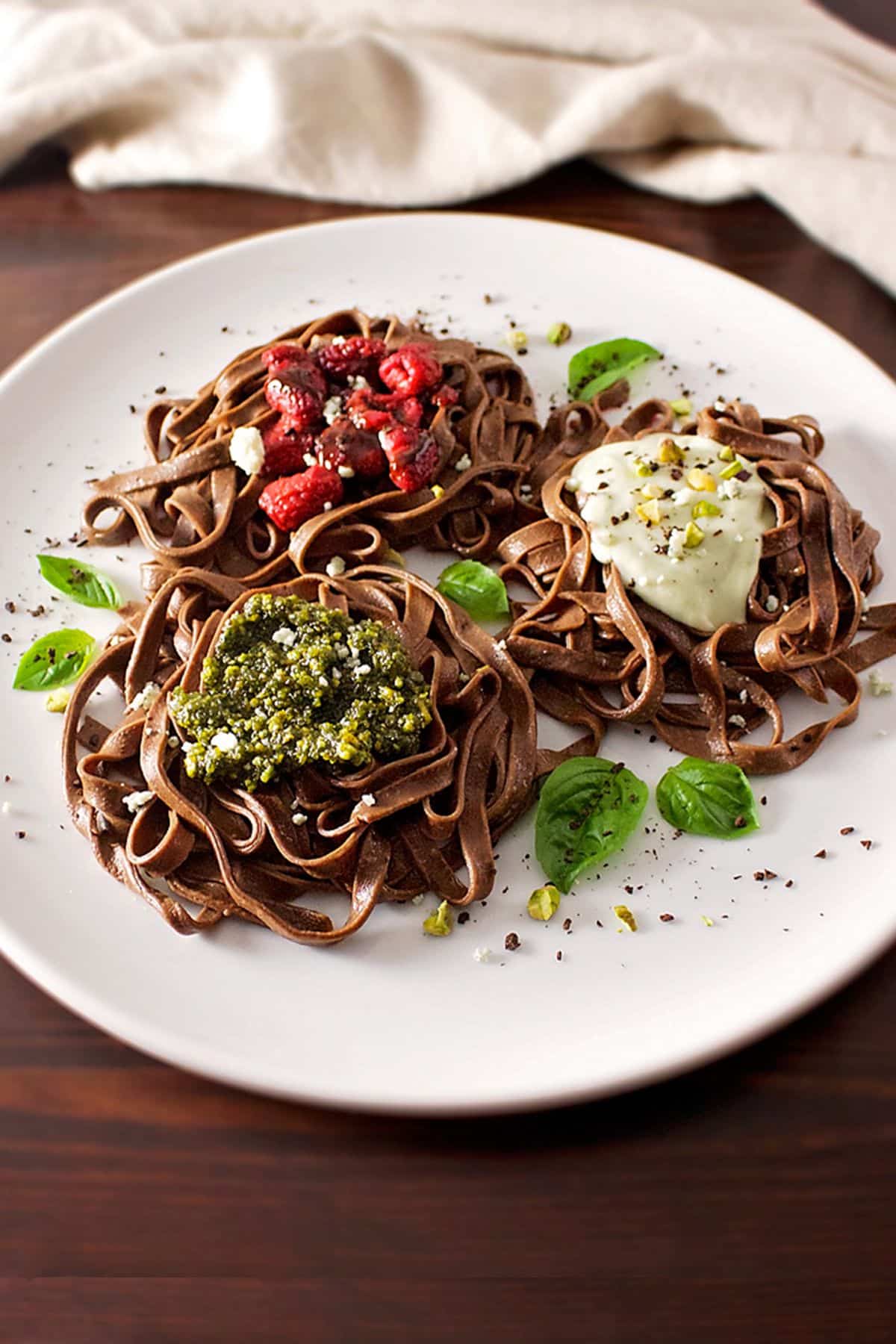 Chocolate Pasta italian dessert with fruits and herbs on a white plate.