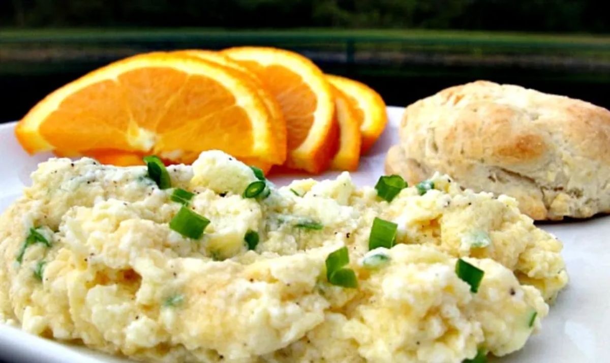 Cottage Cheese Scrambled Eggs with slices of orange and a piece of bread on a white plate.