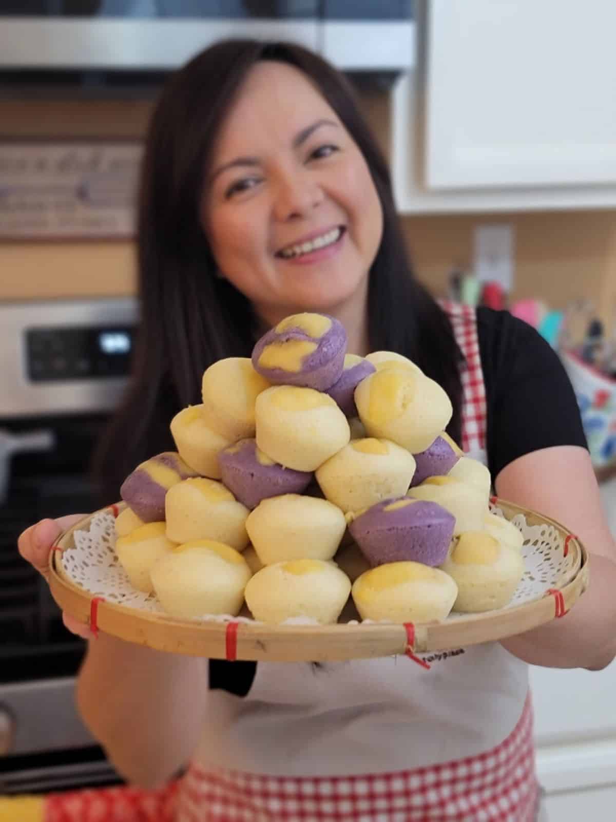 Puto Filipino Desserts stacked on a wooden tray held by a woman.