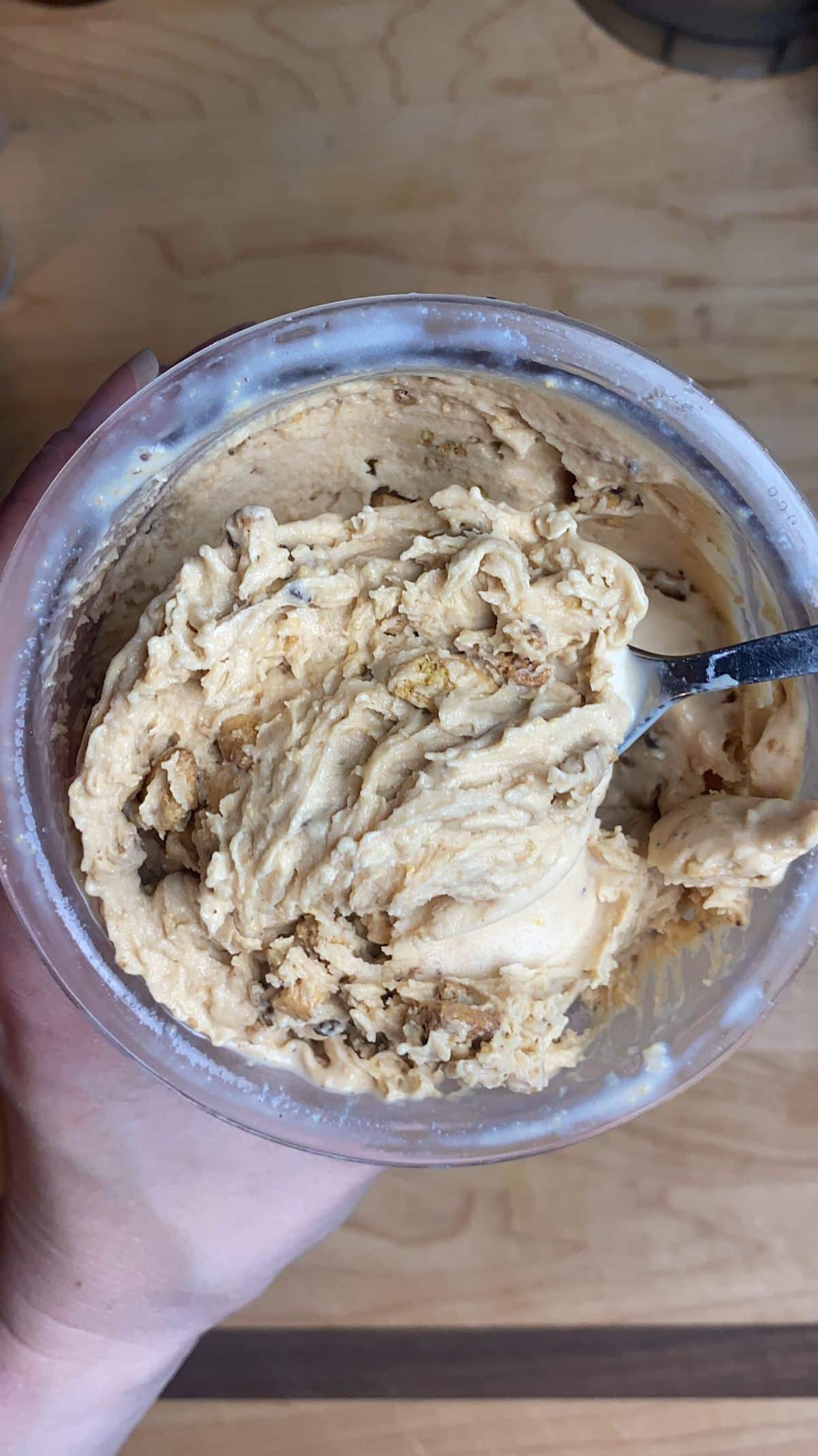 Peanut Butter Crumble Protein Ice Cream in a plastic container with a spoon held by a hand.