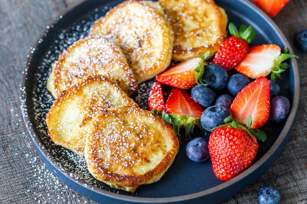 Cottage Cheese Pancakes with fruits on a black pan.