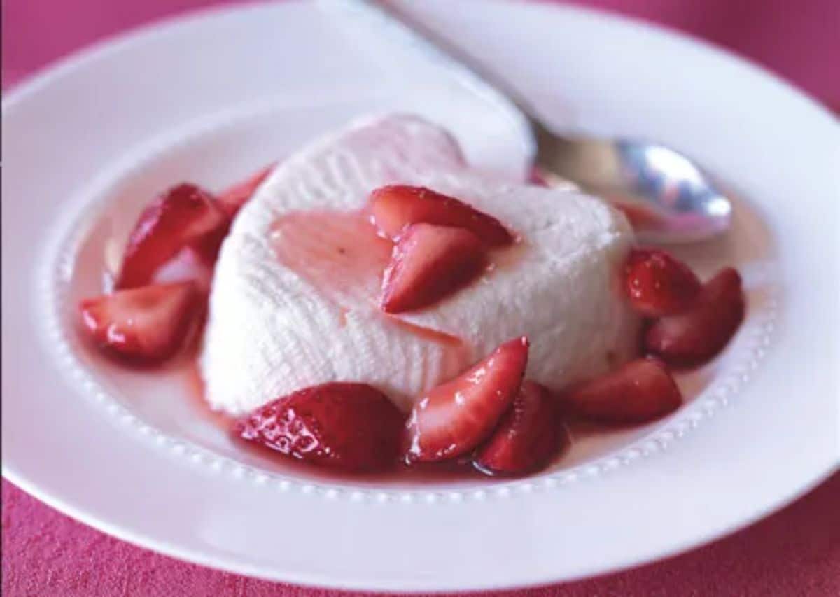 Couer a la Creme with strawberries on a white plate with a spoon.