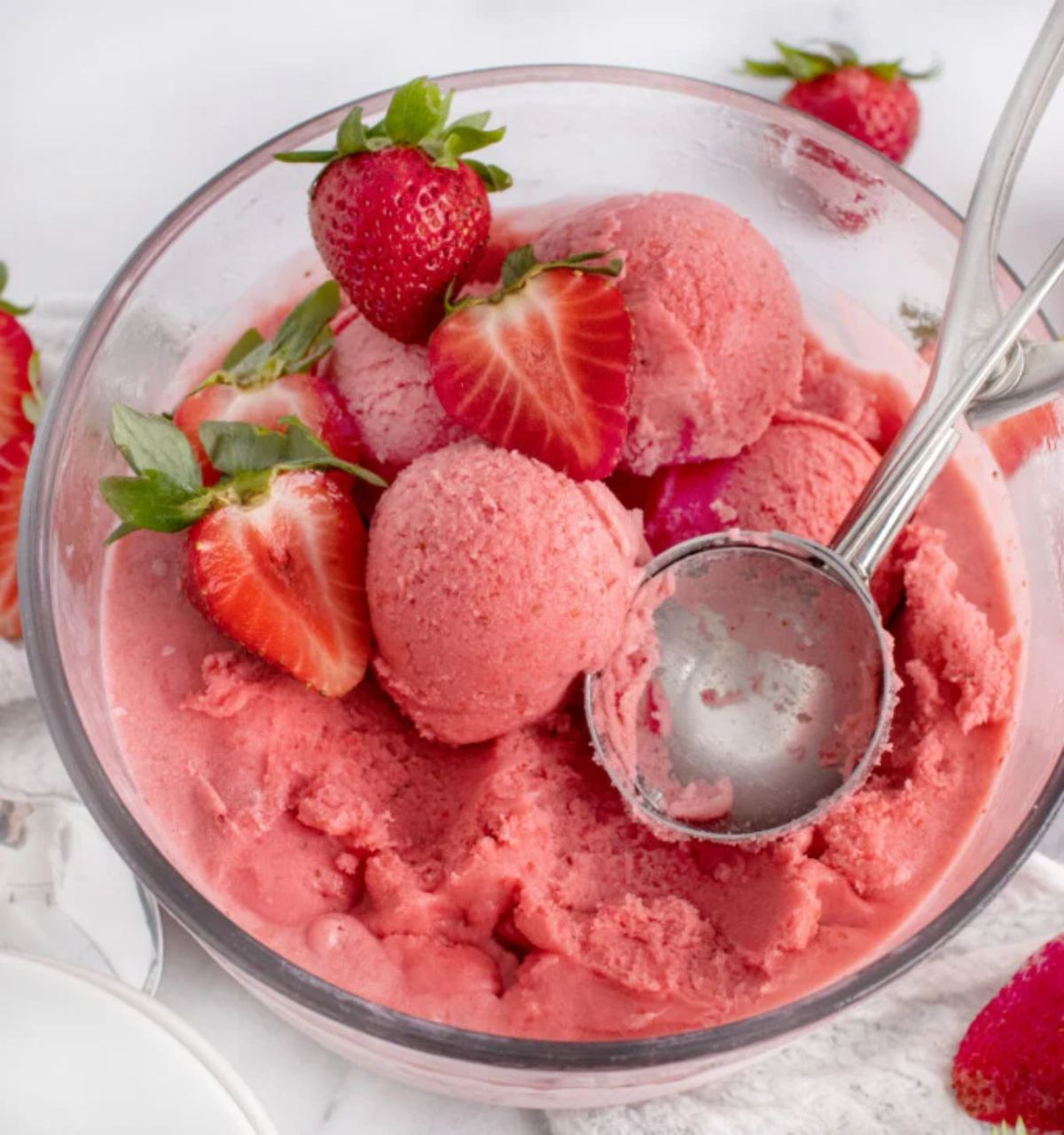 Strawberry Gelato with sliced strawberries in a glass bowl with an ice maker spoon.