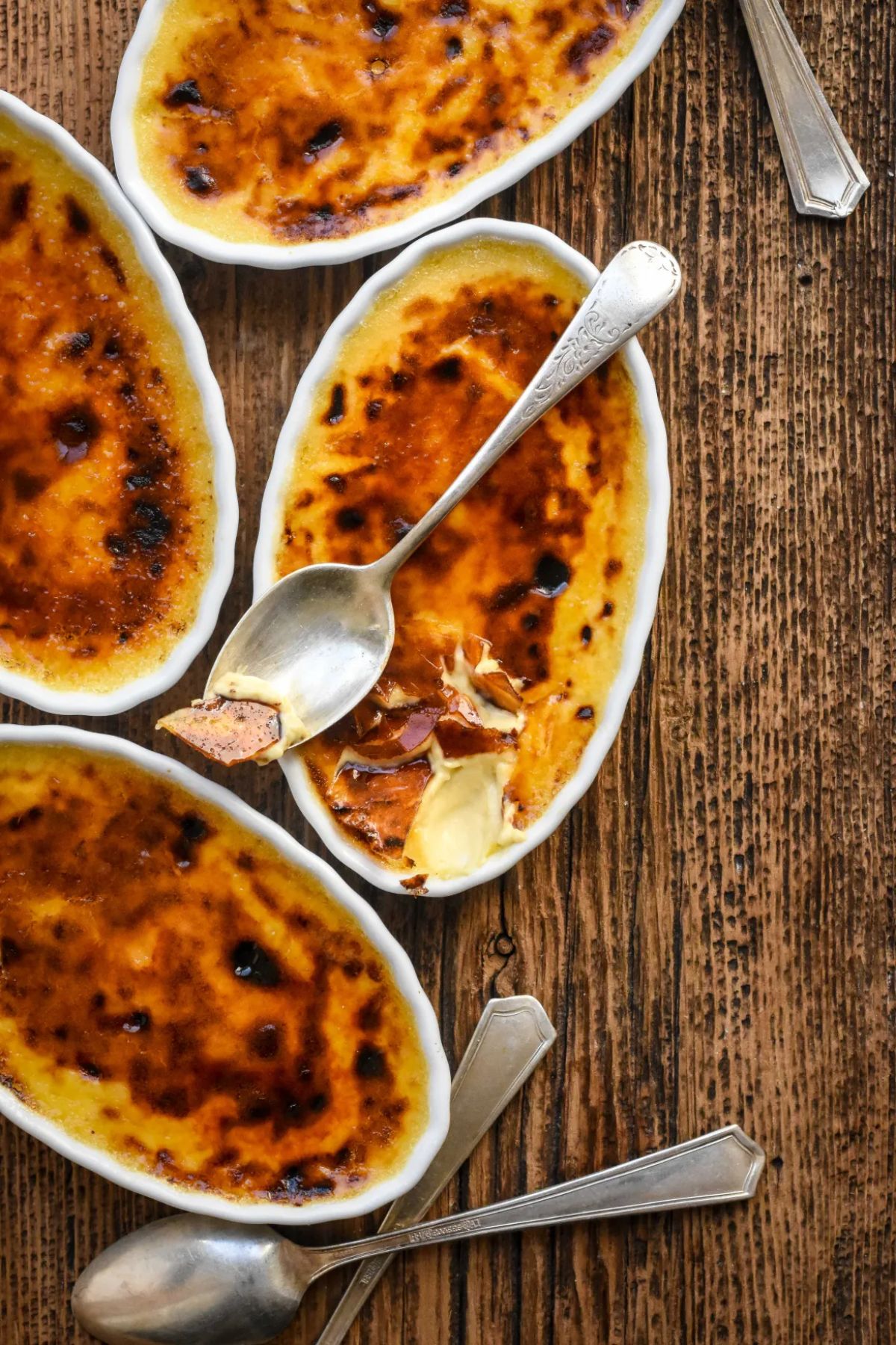 Classic French Creme Brulee in small bowls with spoons on a wooden table.