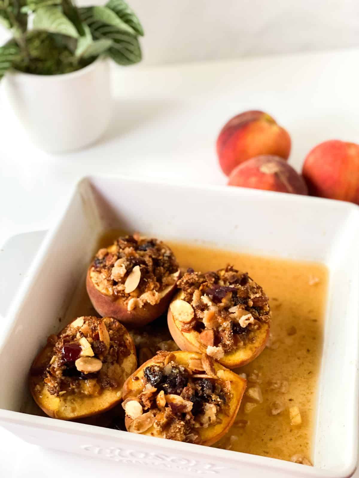 stuffed baked peaches in square white baking dish on white table by small plant