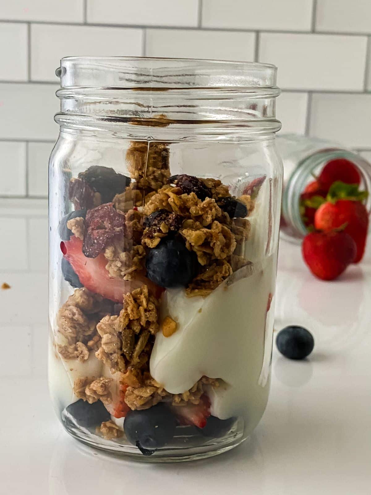 granola, berries, and yogurt layered in tall mason jar on white table