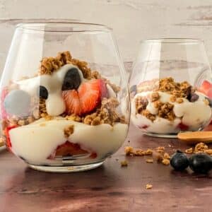 two glasses of yogurt with fruit on wood table in front of white wall