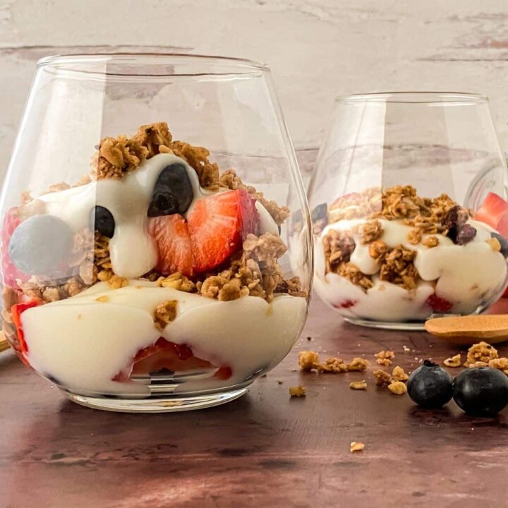 two glasses of yogurt with fruit on wood table in front of white wall